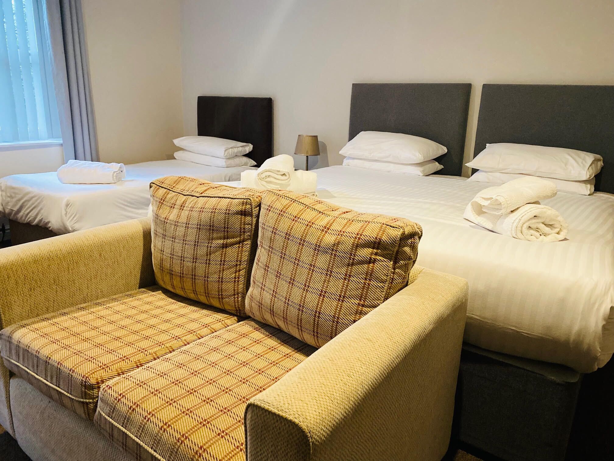 A hotel room with a large bed, two bedside tables, a sofa, and a window with curtains.