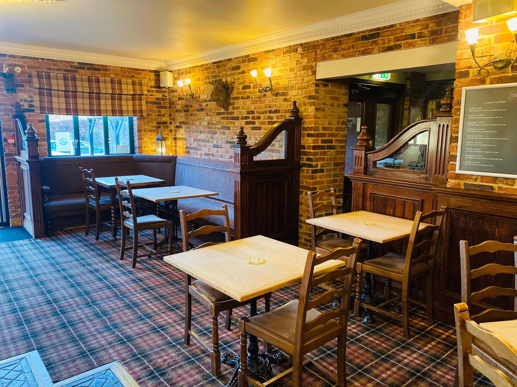 A cozy restaurant with brick walls, wooden tables and chairs, and a plaid-patterned floor.