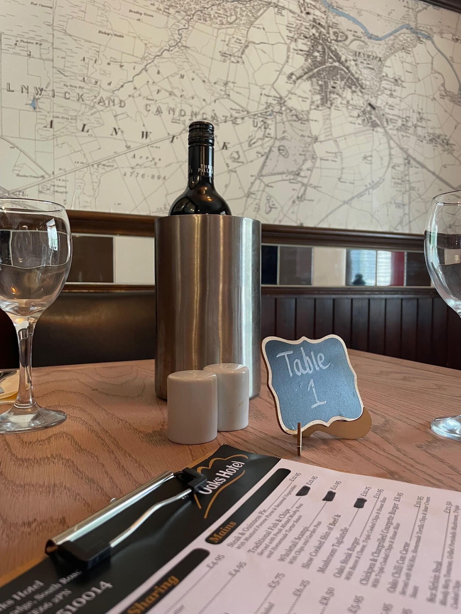 A restaurant table with a menu, a bottle of wine, salt and pepper shakers, and a table number sign.