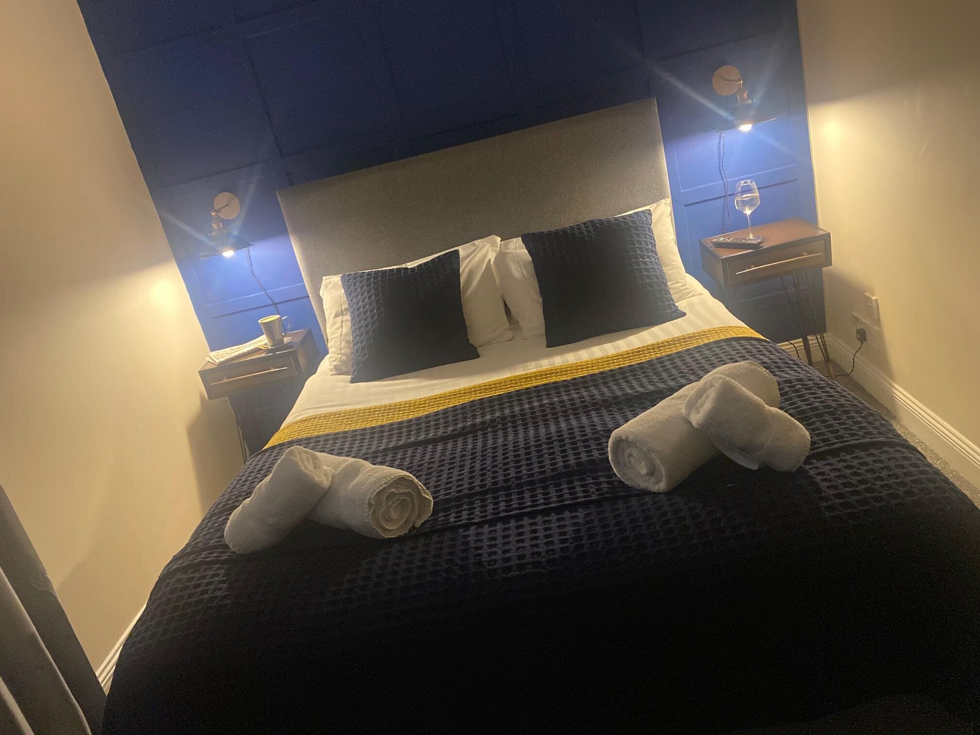 A neatly made bed with a dark blue and white checkered bedspread, two pillows, and two rolled towels.