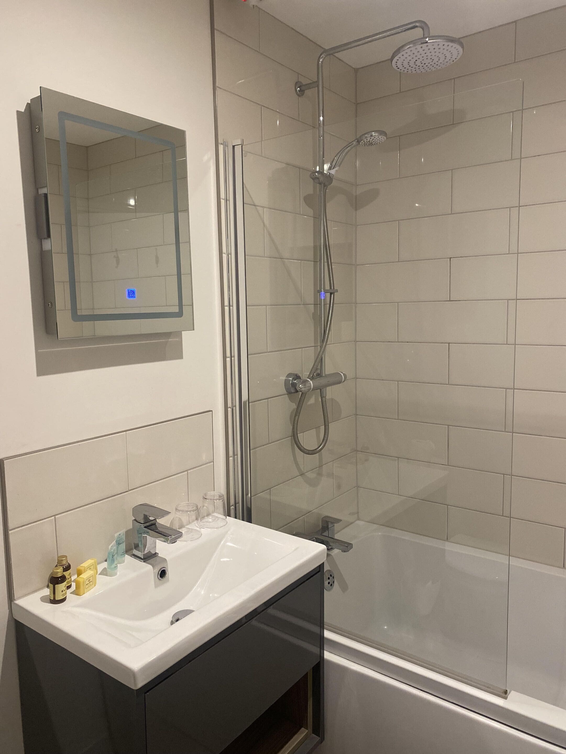 A modern bathroom with a glass-enclosed shower, a white sink with toiletries, and a mirror above the sink.