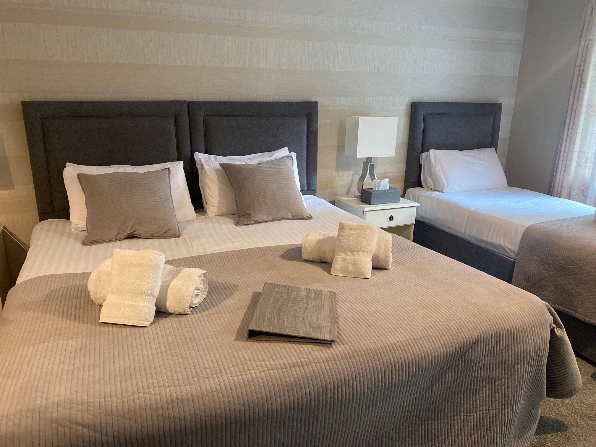 A hotel room with two beds, each with a headboard, a bedside table with a lamp, and a small box of tissues.