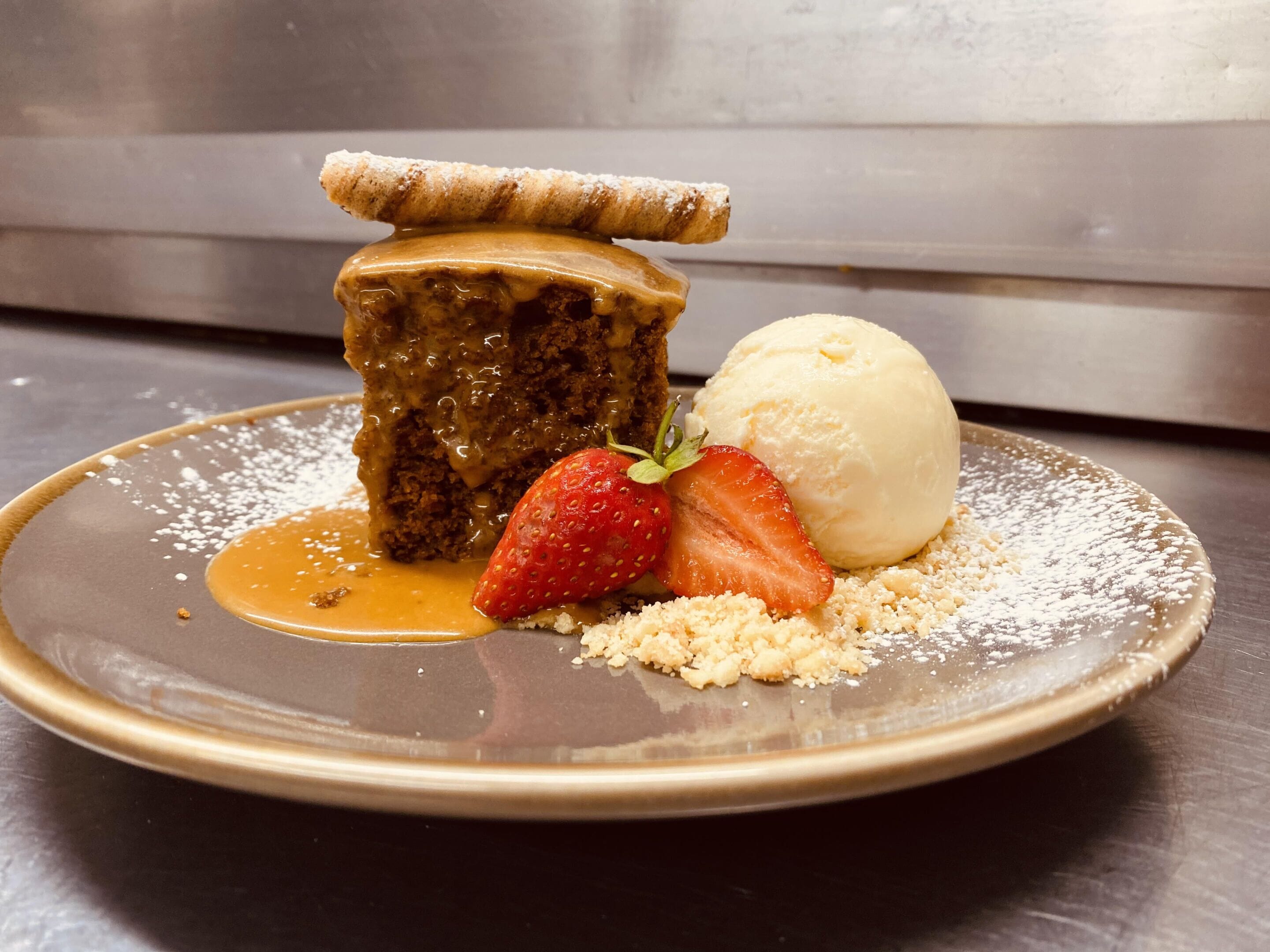 Un plato de postre con una porción de pastel, una bola de helado y una fresa.