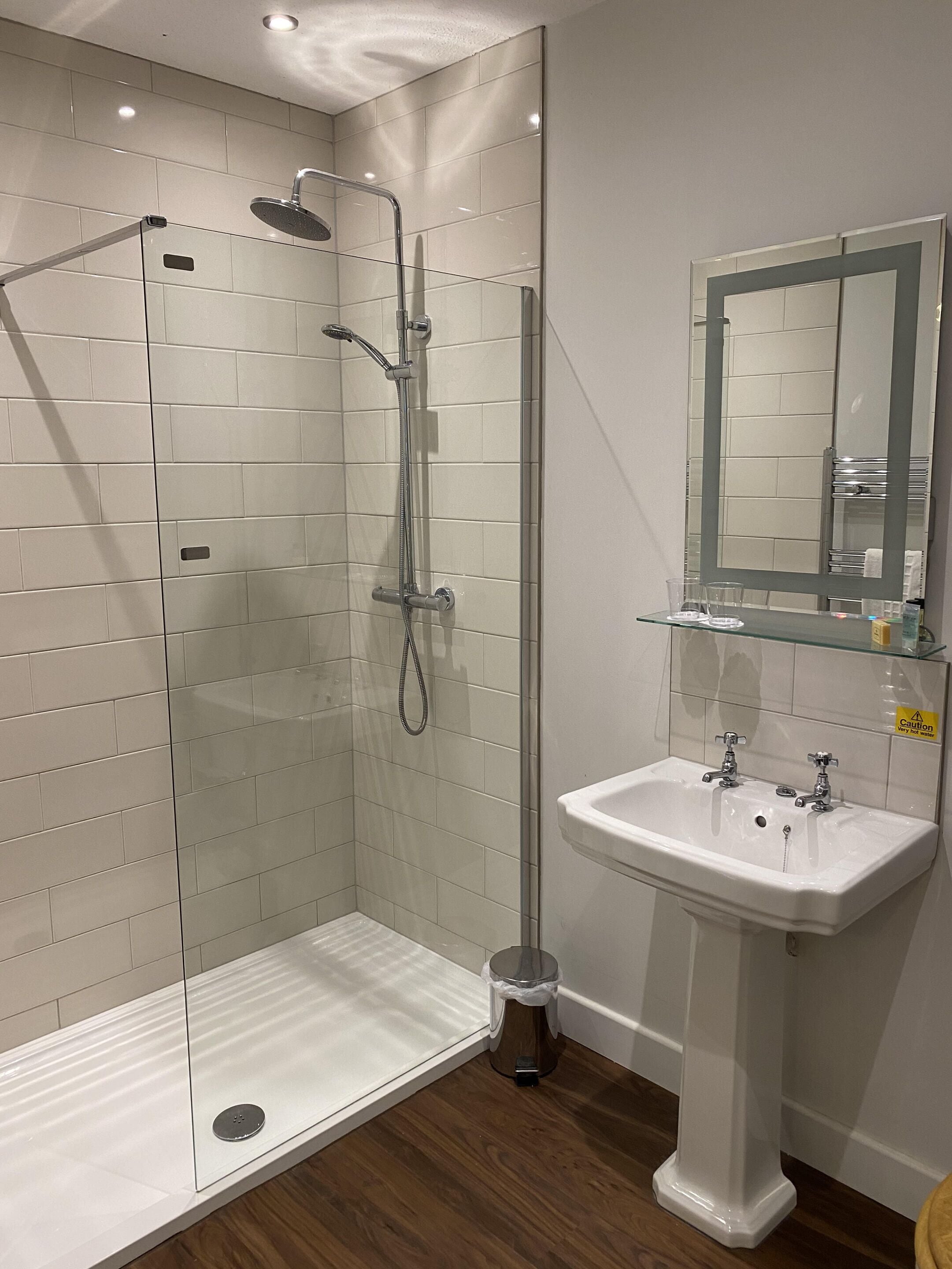 Un baño moderno con ducha envuelta en vidrio, un lavabo pedestal blanco y un espejo sobre el lavabo.