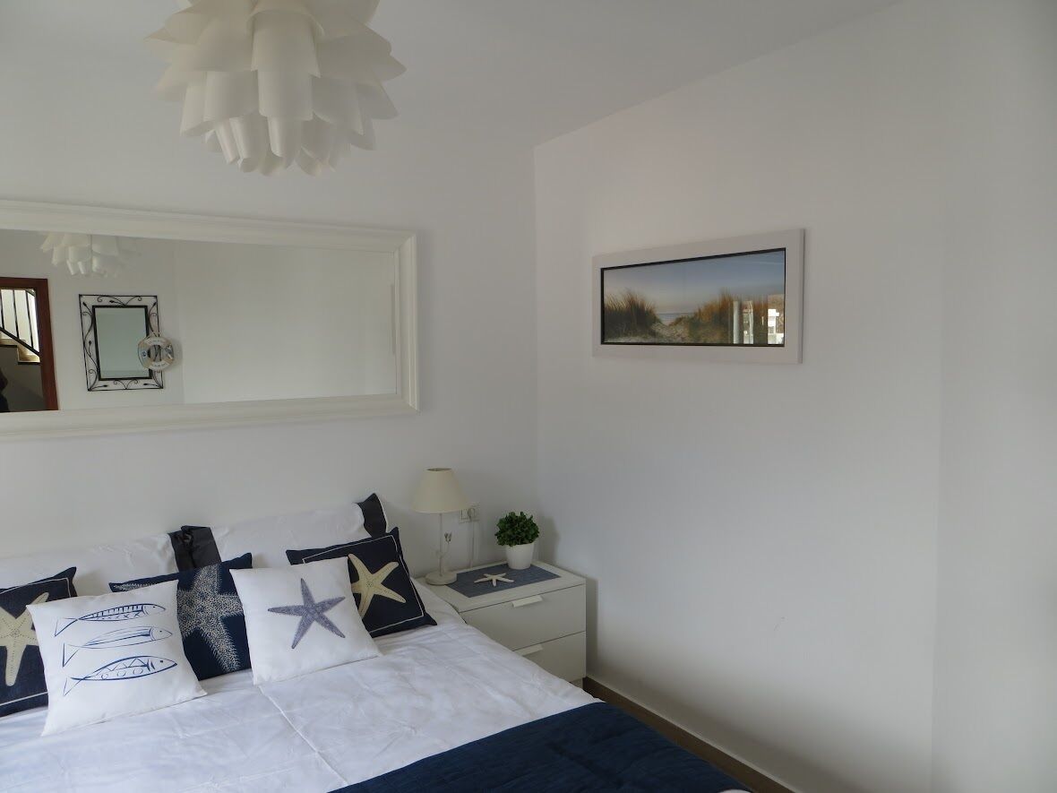 A bedroom with a bed, a nightstand, a lamp, a framed picture, and a mirror on the wall.