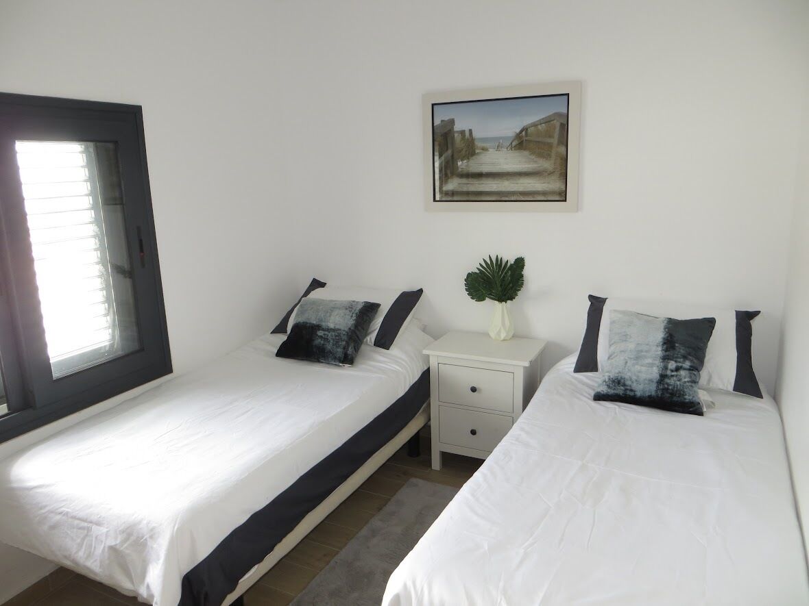 Una camera da letto con due letti, un comodino, una piccola pianta e un quadro appeso al muro.