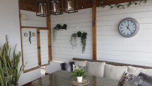 Una habitación acogedora con techo de madera, una mesa de vidrio con planta en maceta, un sofá con cojines y un reloj fijado a la pared.