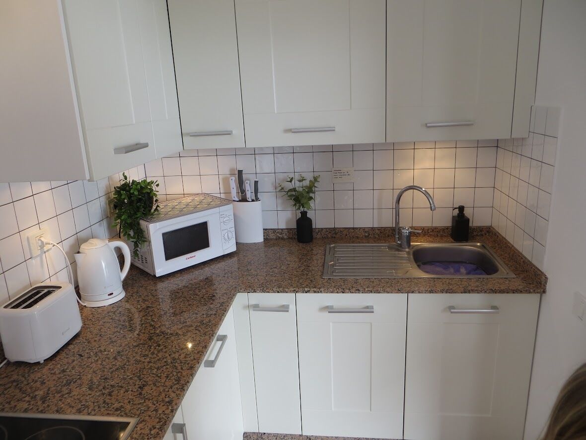 A modern kitchen with white cabinets, a granite countertop, a microwave, a coffee maker, and a sink.
