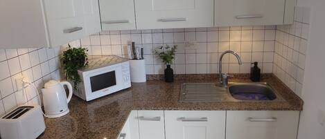 A modern kitchen with white cabinets, a granite countertop, a microwave, a coffee maker, and a sink.