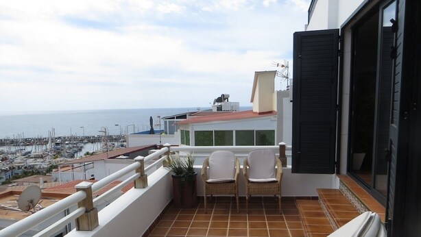 Un balcón con vista al mar, dos sillones de mimbre y una tumbona.