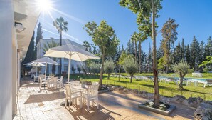 Une terrasse extérieure avec des chaises blanches et des parasols, entourée d’arbres et d’une pelouse.