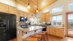 Une cuisine avec des meubles de rangement en bois, un réfrigérateur noir, un plan de travail en granit et des tabourets en bois.