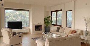 Un salon moderne doté d’une cheminée, d’un téléviseur et de grandes fenêtres donnant sur une colline.