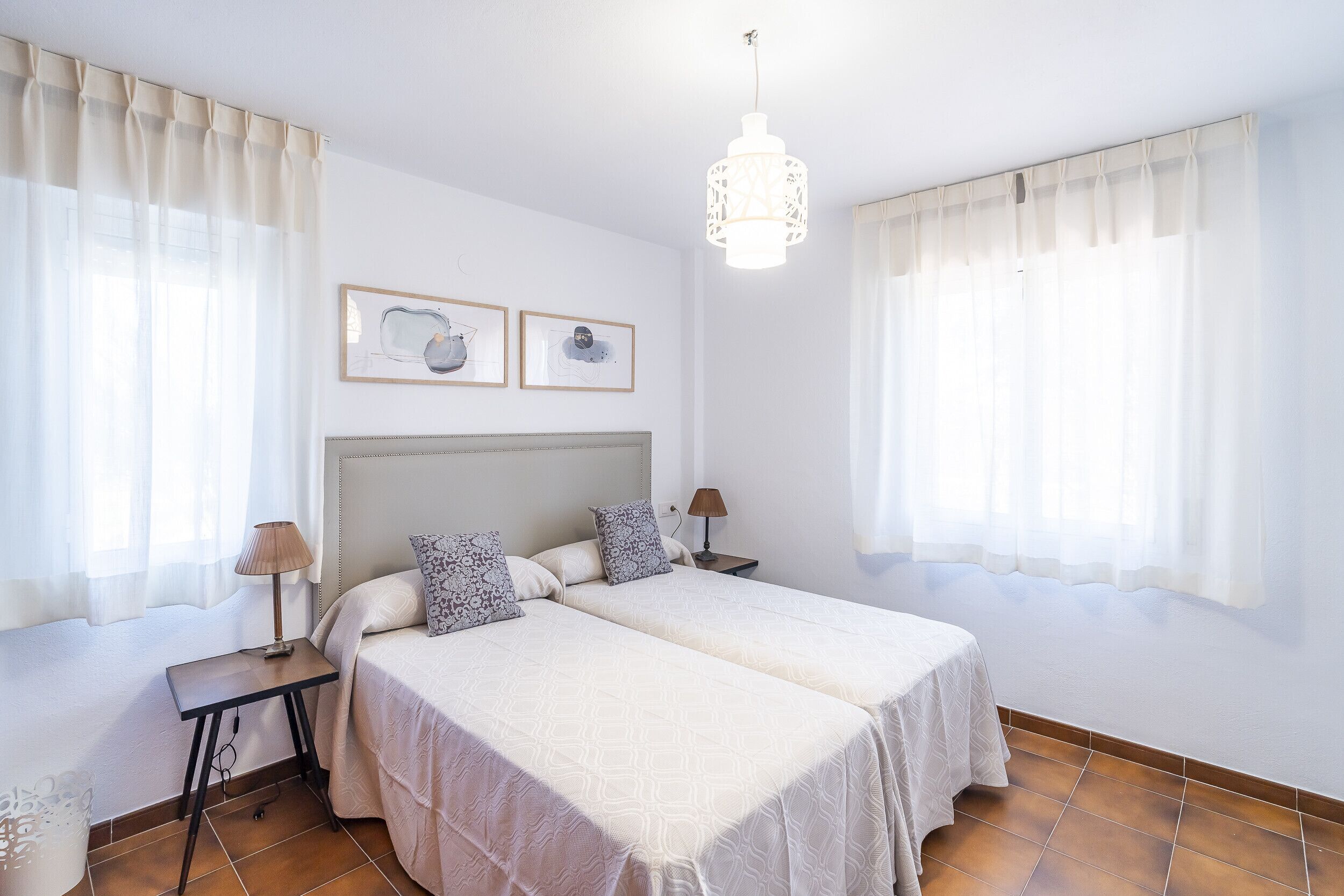 A double room with two beds, a headboard, bedside tables, a lamp, and artwork on the wall.