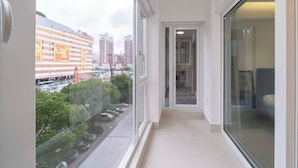 A narrow corridor with a glass door leading to a room, a view of a cityscape with buildings and a road, and a balcony with a view of the road and greenery. - Book and Bed-Chang Ning (Shanghai)