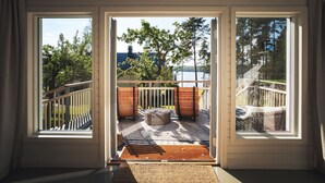 Et værelse med store vinduer, en træterrasse, udendørs møbler og udsigt til træer og vand.