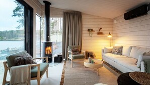 En hyggelig stue med pejs, trævægge, sofa, stole og udsigt til en sø.