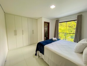 A bedroom with a bed, a wardrobe, a window with curtains, and a view of greenery.