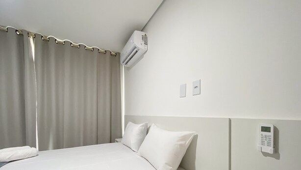 A hotel room with a bed, a wall-mounted air conditioner, a bedside table, and a control panel on the wall. - Residencial Jardins de Taperapuã 2 (Porto Seguro)