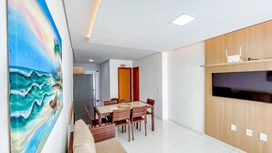 A modern living room with a dining area, a large painting, and a TV on the wall.