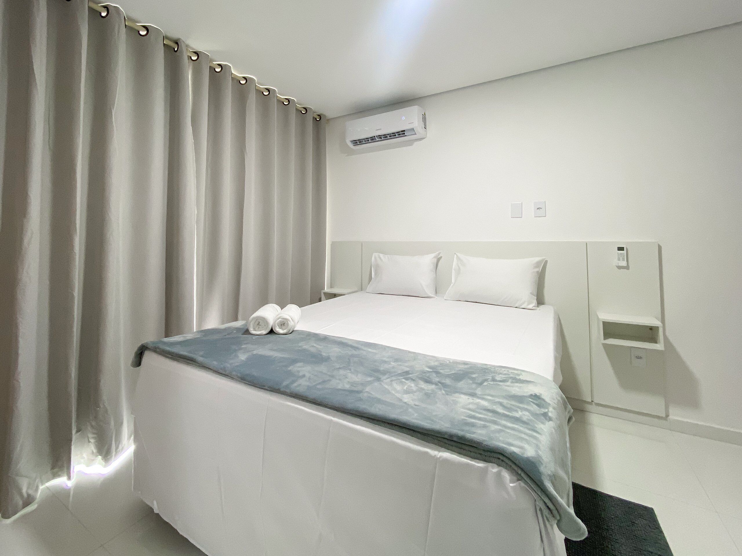 Camera d'albergo con un letto, tende, un condizionatore, un comodino e un pannello di controllo a parete.