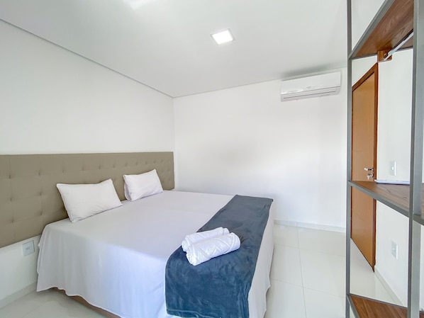 A hotel room with a bed, a bedside table, an air conditioning unit, and a wooden door.