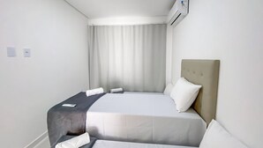 A hotel room with a bed, a bedside table, a wall-mounted air conditioner, and a window with curtains. - Residencial Jardins de Taperapuã 2 (Porto Seguro)