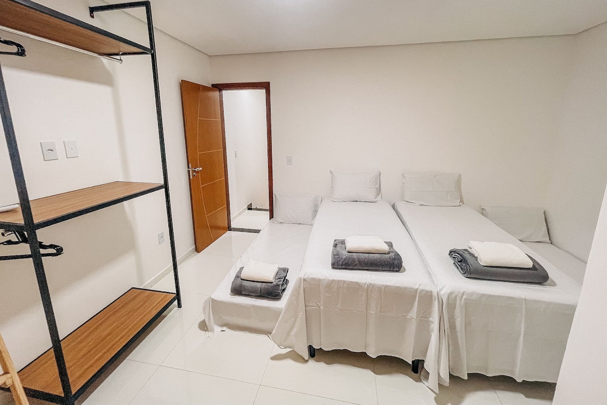 A room with two beds, a wooden shelf unit, and a door leading to another room.