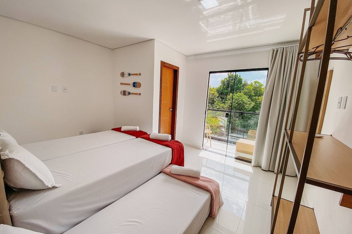 A bedroom with two beds, a balcony with a view, and a wooden wardrobe.