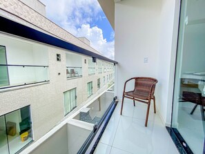 A balcony with a wicker chair, a glass door, and a view of a building with multiple windows.