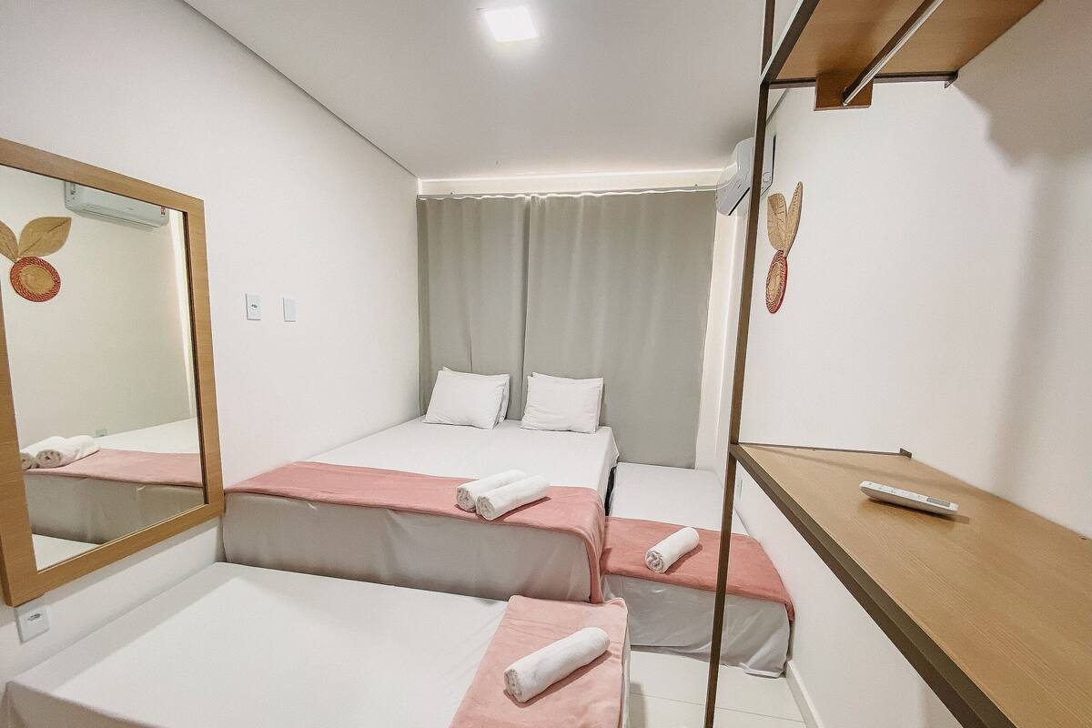A hotel room with two beds, a mirror, a wooden desk, and a remote control.