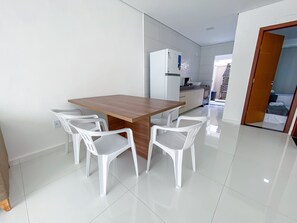 A modern kitchen with white cabinets, a wooden dining table, and four white chairs. - Residencial Jardins de Taperapuã 2 (Porto Seguro)