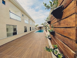 Un edificio moderno con piscina, una pared de madera con macetas y un patio con baldosas.