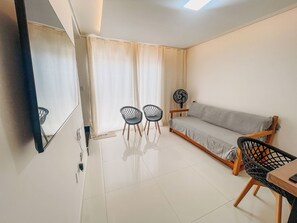 A modern living room with a sofa, two chairs, a fan, and a dining table. - Residencial Jardins de Taperapuã 2 (Porto Seguro)
