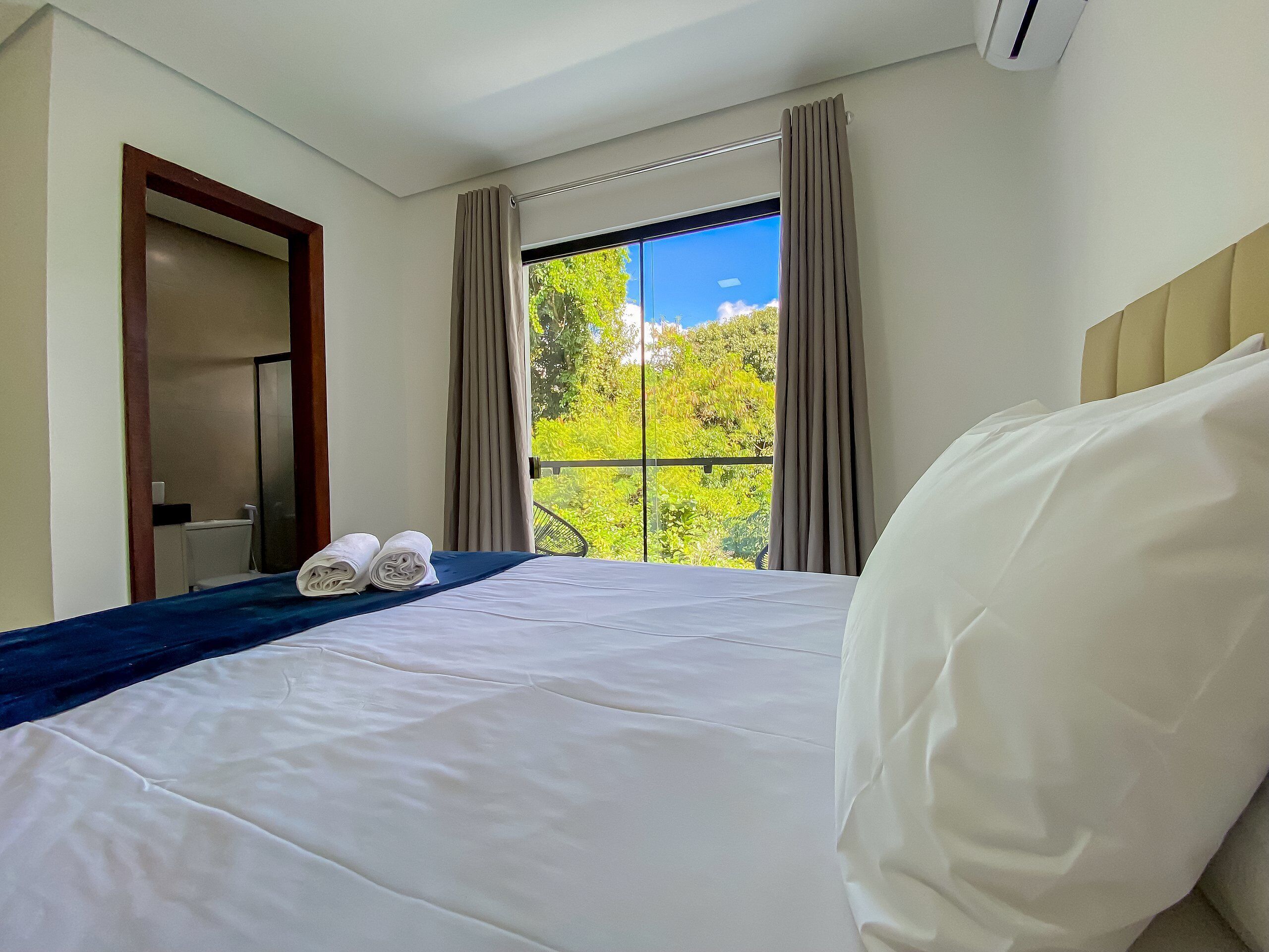 Une chambre d’hôtel avec un lit, une fenêtre avec des rideaux, une vue sur la verdure et un appareil de climatisation.