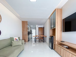Una sala de estar moderna con un sofá, televisor y una zona de comedor con sillas y una mesa.