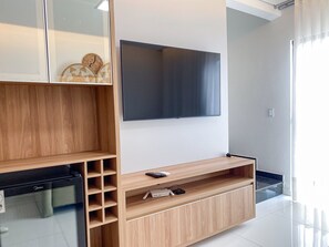 A modern living room with a large flat-screen TV mounted on the wall, wooden shelving units, and a built-in entertainment center. - Residencial Jardins de Taperapuã 2 (Porto Seguro)