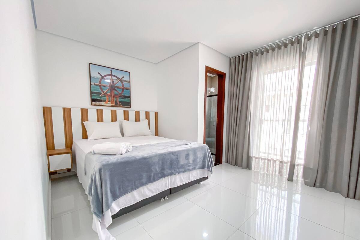 A hotel room with a bed, a painting, a door, and a window with curtains.
