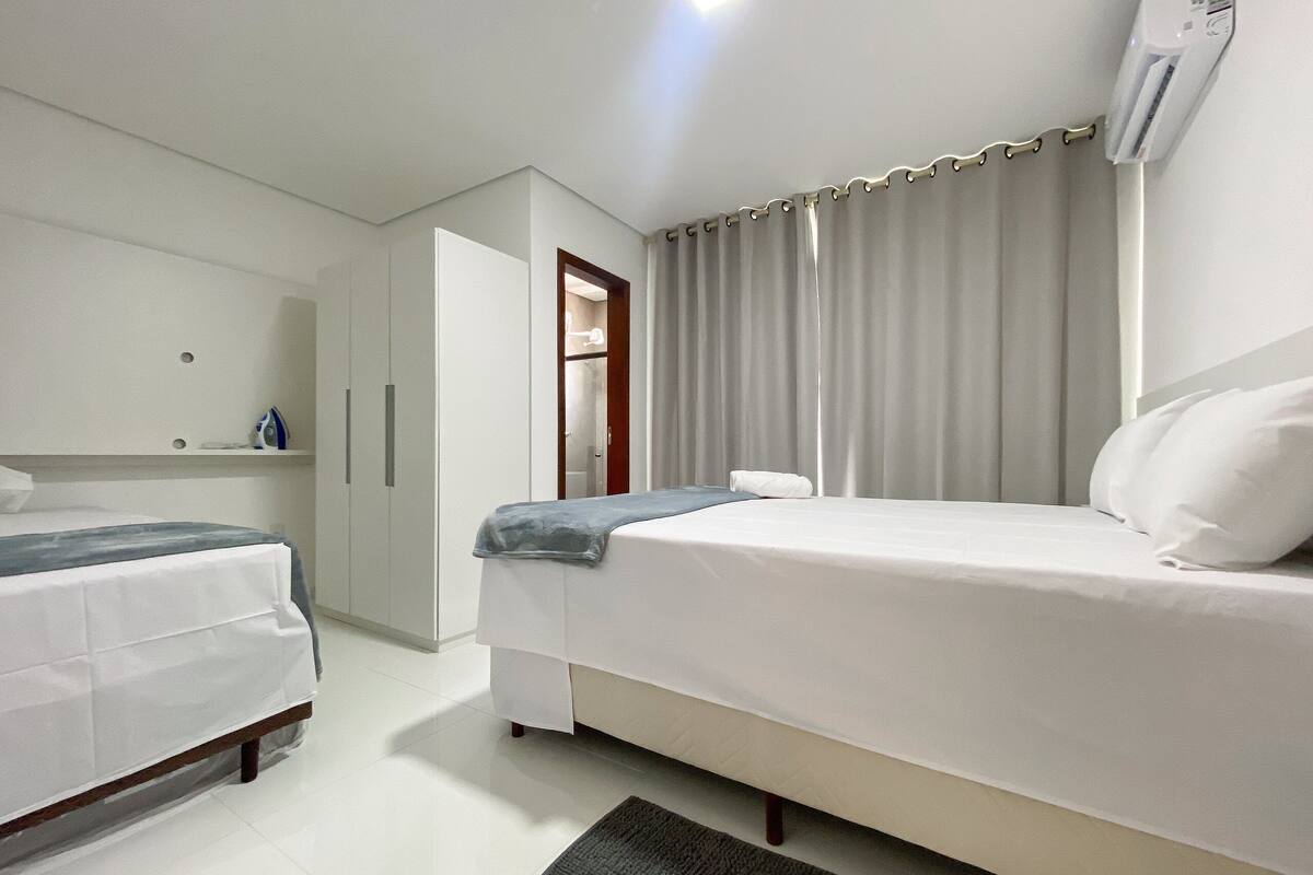A hotel room with a bed, a wardrobe, a mirror, and a window with curtains.