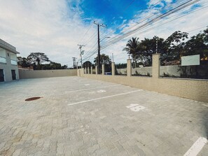 A paved parking area with marked spaces, a building on the left, and utility poles with wires. - Residencial Jardins de Taperapuã 2 (Porto Seguro)
