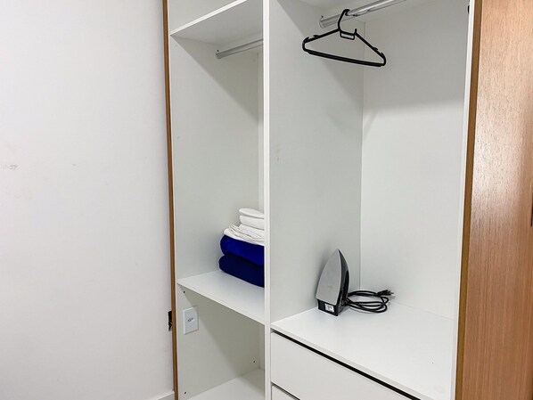 A white closet with a hanging rod, a folded blue towel, and a black electronic device on the shelf.