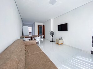 Uma sala de estar moderna com um sofá, uma mesa de jantar, cadeiras, uma TV, um ventilador e um pequeno armário.