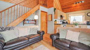A cozy cabin interior with a wooden staircase, two leather sofas, a kitchen area, and a dining table. - Cornish Woodland Retreat (Bodmin)