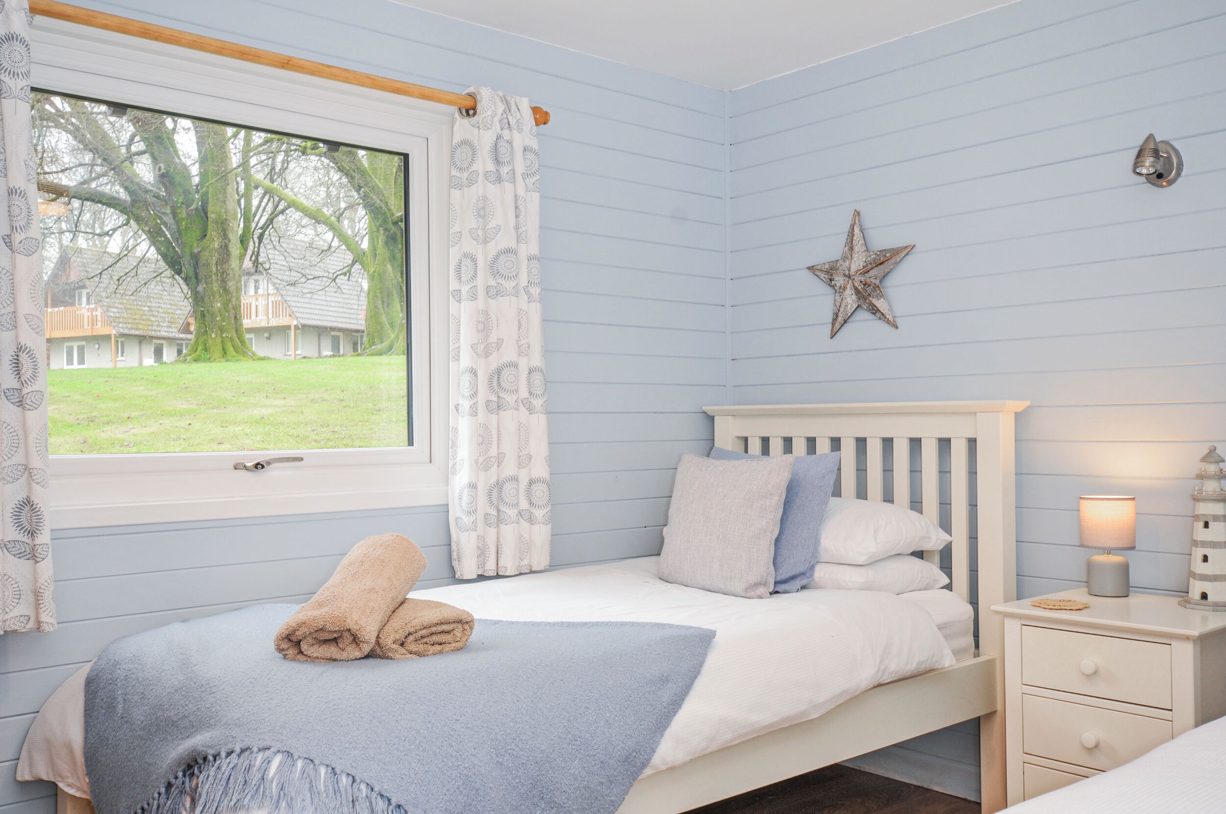 A bedroom with a bed, a nightstand, a lamp, a star decoration, and a window with curtains.