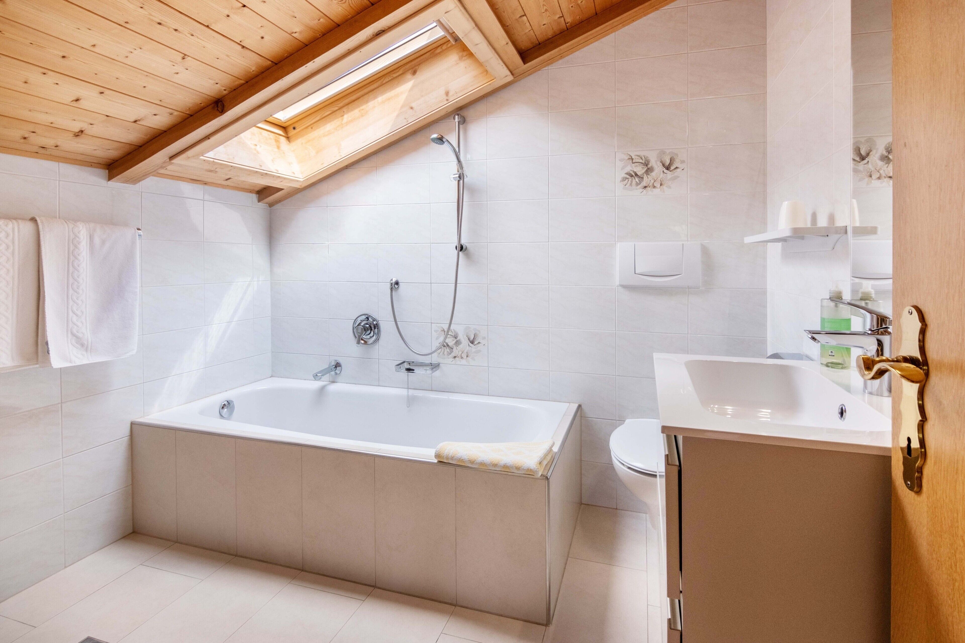 A modern bathroom with a skylight, a bathtub, a toilet, and a sink.