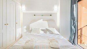 Quarto com cama, guarda-roupa branco e janela com vista.