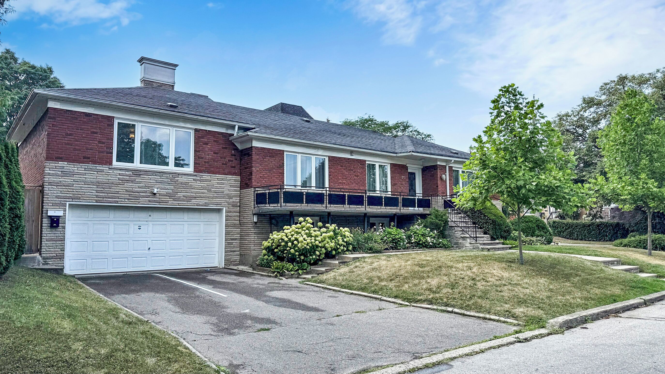 A two-story brick house with a white garage door, a covered front porch, and a well-maintained lawn.