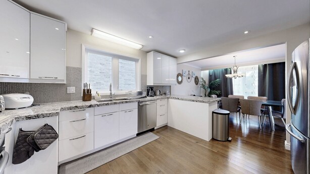 Una cocina moderna con armarios blancos, encimera de granito y un comedor con mesa y sillas.