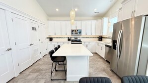 A modern kitchen with white cabinets, a central island, black chairs, and a stainless steel refrigerator. - Beach Block Downtown Luxury Walk to Everything! (Sea Isle City)