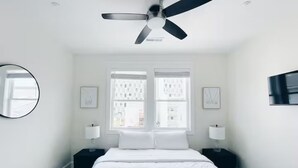 A bedroom with a bed, two bedside tables, a ceiling fan, and two windows. - Beach Block Downtown Luxury Walk to Everything! (Sea Isle City)